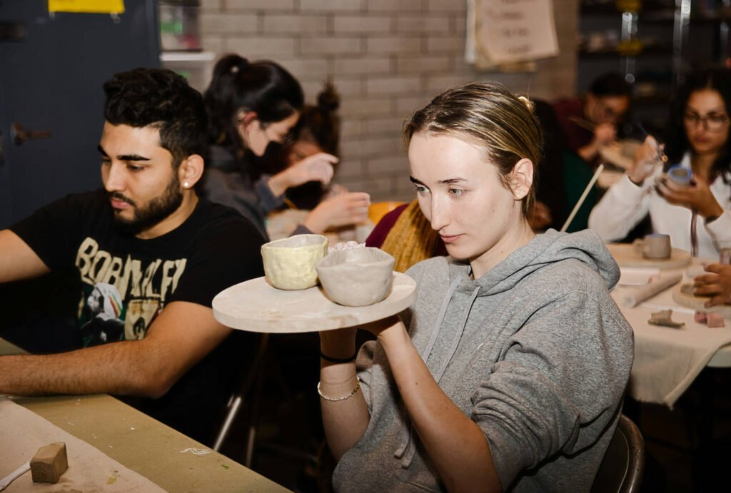 Student holding ceramic bowls during a practical art portfolio workshop with peers working in clay.