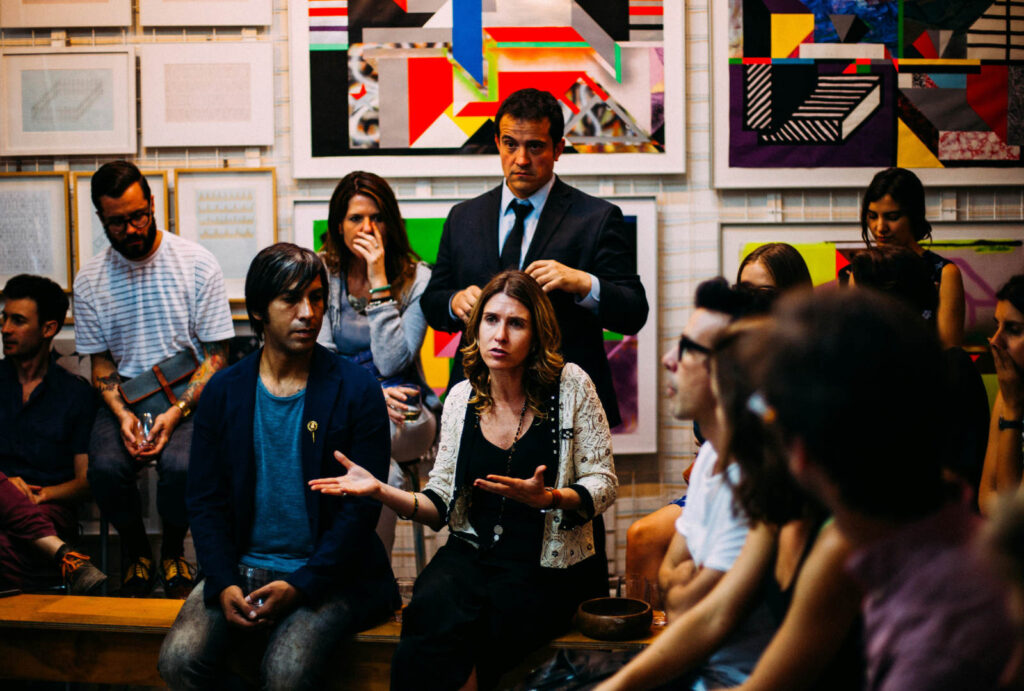 Group critique in a gallery setting with students and artists discussing work surrounded by colourful abstract paintings.