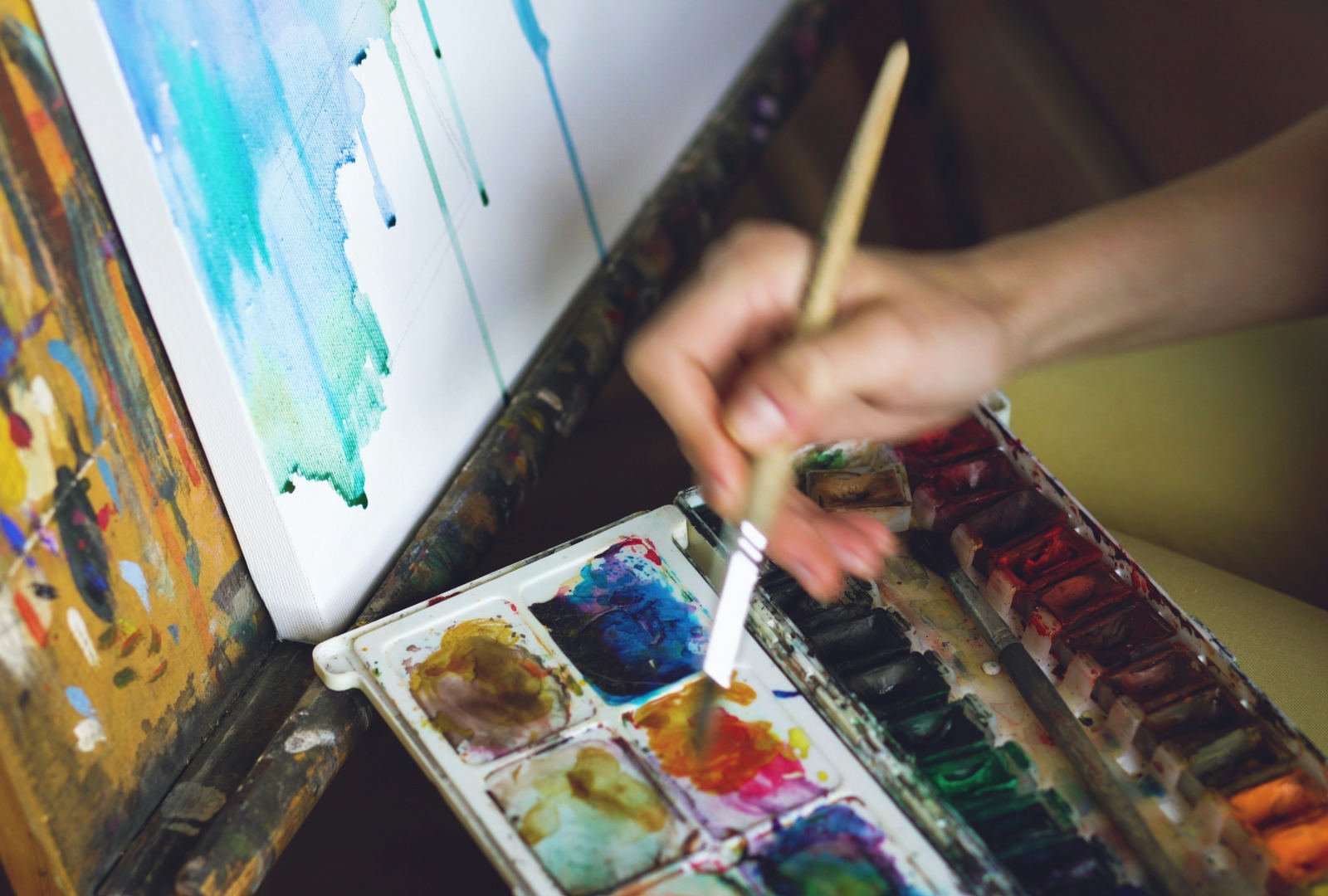 Hand painting with watercolour beside a canvas, suggesting process-led work for a Parsons BFA Fine Arts portfolio.