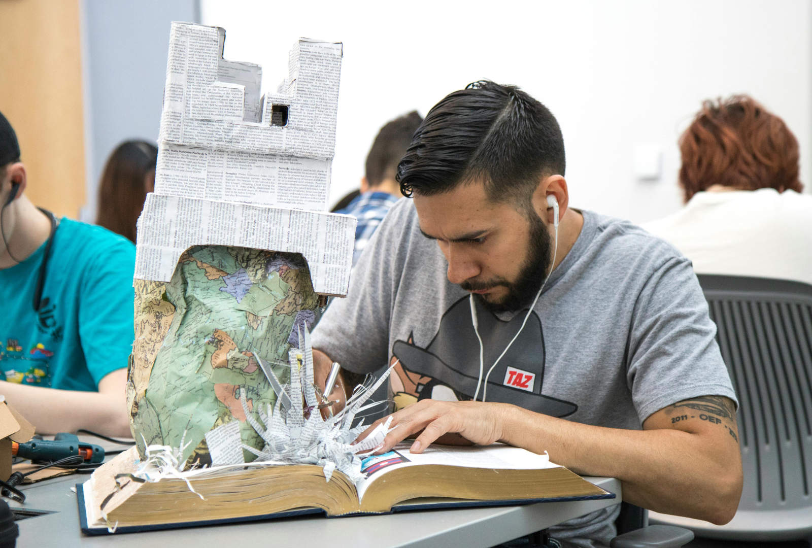 Student working beside an experimental paper and map sculpture emerging from an open book.