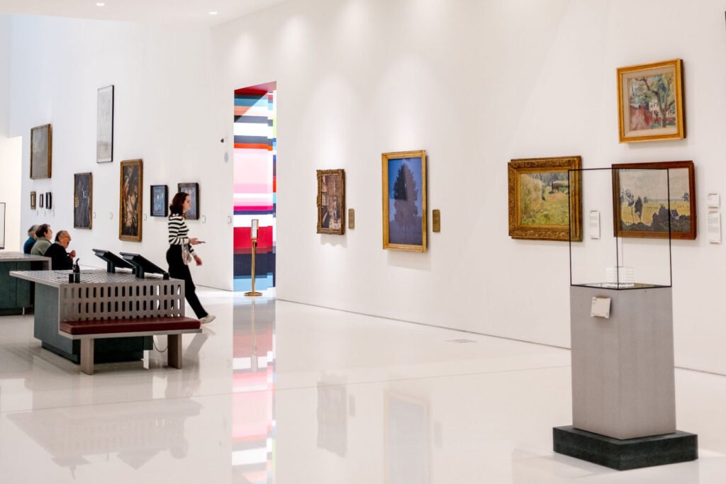 White-walled gallery interior with paintings, a display case and visitors, reflecting the professional context of MA Art Business study.