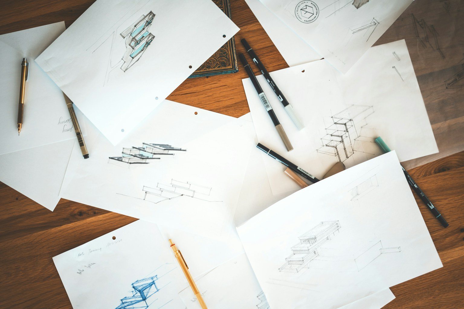 Drawings from an art portfolio spread across a wooden table with pens, ready for an art portfolio review