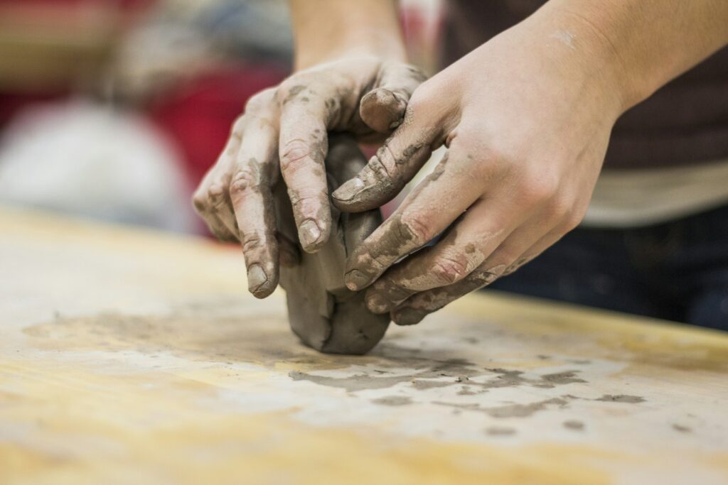 Clay-covered hands shaping a lump of clay on a work table, for applicants preparing a Falmouth Fine Art portfolio