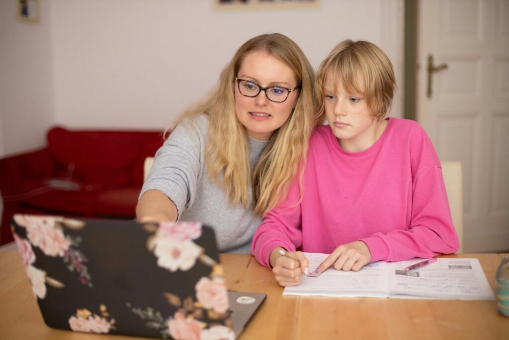 A parent and teenager at a table with a laptop and notebook, working through art school applications together