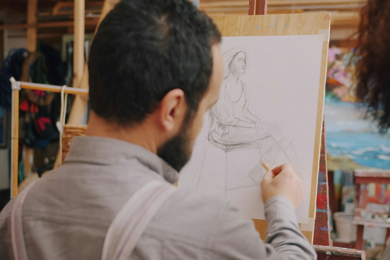 Person sketching a seated figure on paper clipped to a wooden easel, illustrating our guide to the Yale art supplement