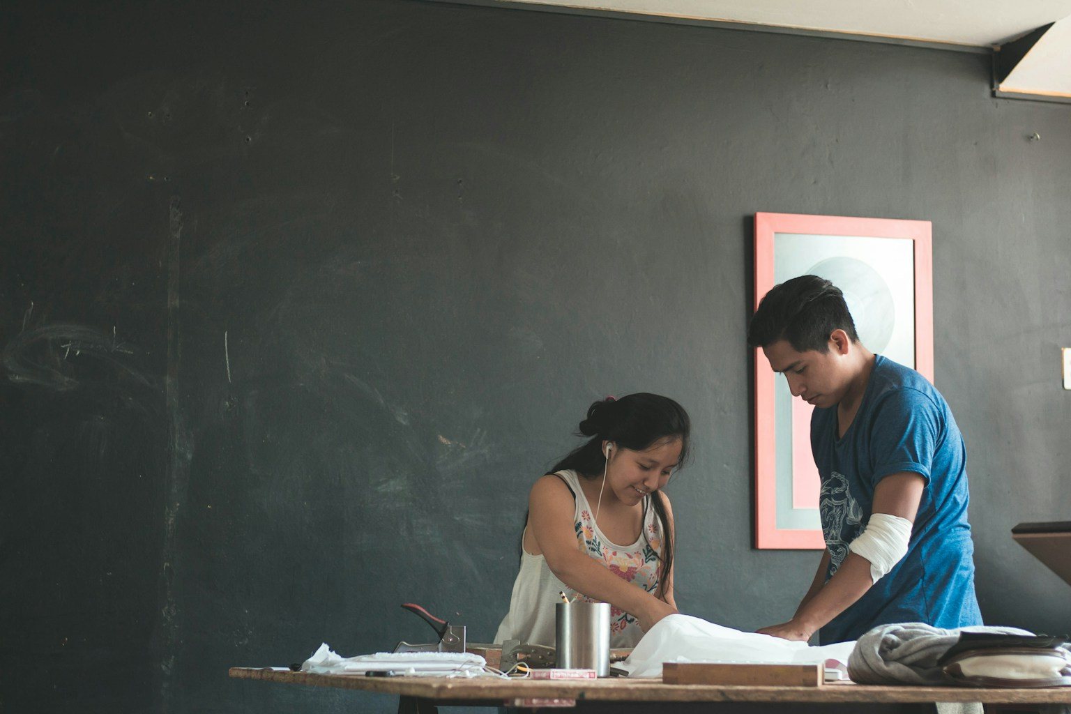 Two people working together at a table in an art studio with a dark wall