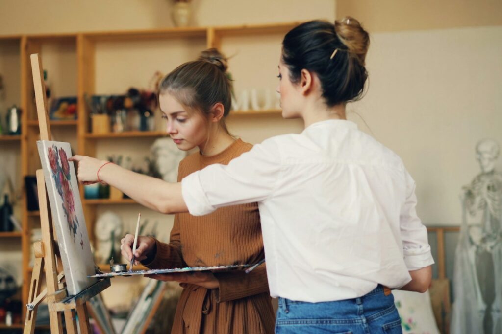 Two women working together on a painting at an easel in a bright studio, illustrating our guide on whether UK art schools are worth it