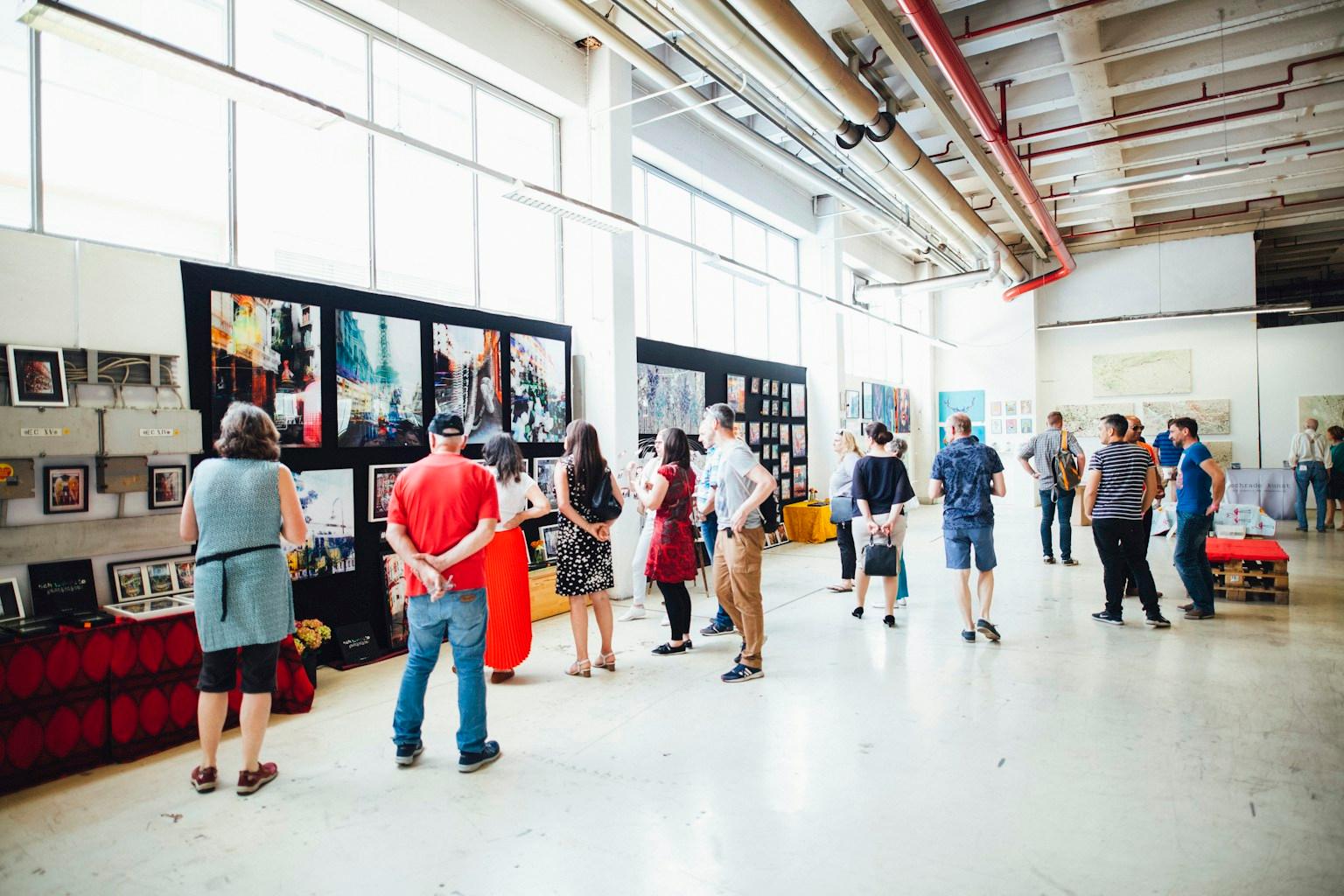 Visitors at a busy art exhibition in a bright hall, looking at the work on the walls