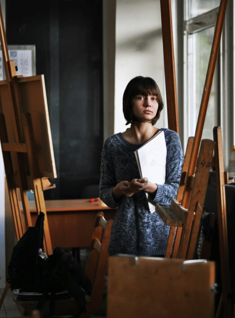 Young woman holding a book among wooden easels in a painting studio, for applicants meeting the Royal Academy Schools portfolio requirements